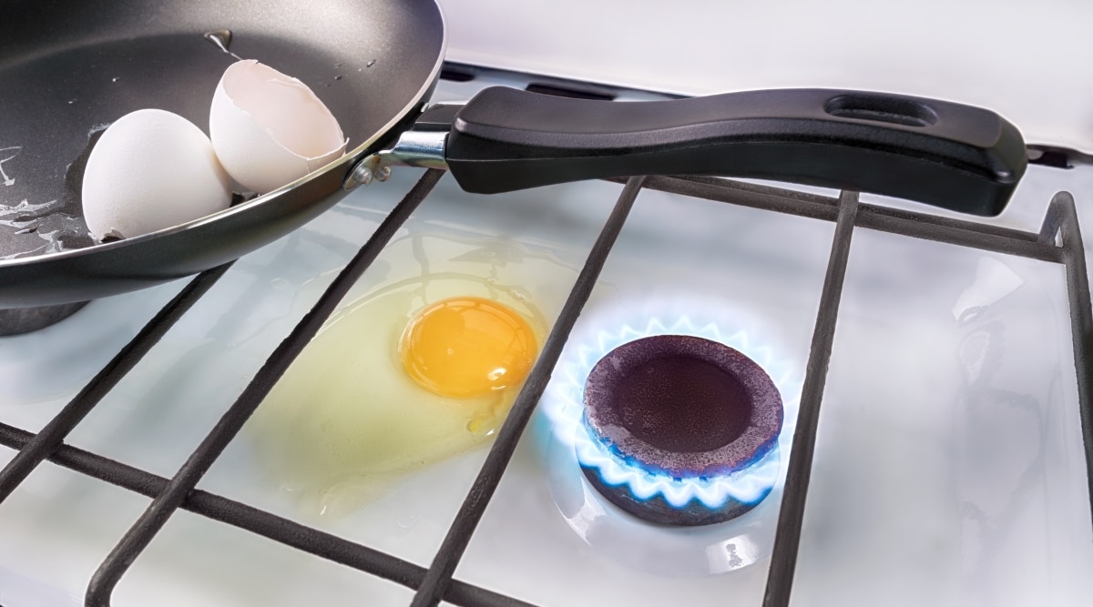 Eggs cooking on a stove with egg next to the blue flame from the gas